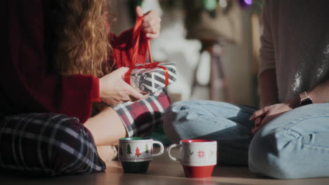 woman opening christmas present given by sister while sitting on floor at home