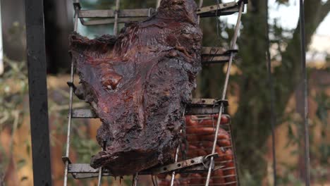 static close-up of steak and sausages hanging at an angle over glowing grill. clip captures slow cooking process and rustic barbecue setup