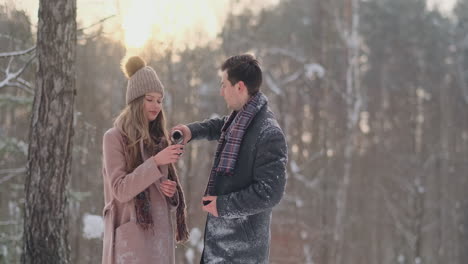 Verliebtes-Paar-Im-Winterwald,-Um-Tee-Aus-Einer-Thermoskanne-Zu-Trinken.-Stilvoller-Mann-Und-Frau-In-Einem-Mantel-Im-Park-Im-Winter-Für-Einen-Spaziergang.