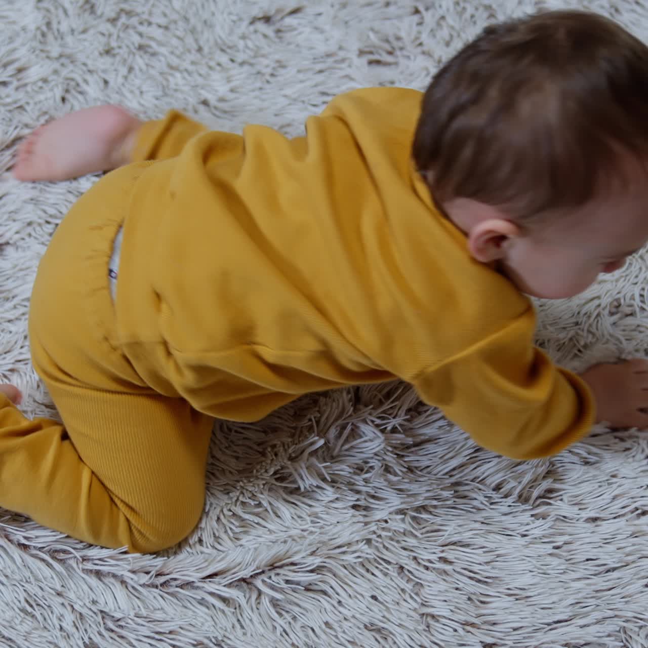 Lovely Caucasian boy lies on the fluffy plaid. Mom's hand reach the kid and tickle him. Baby stands on all four and crawls away