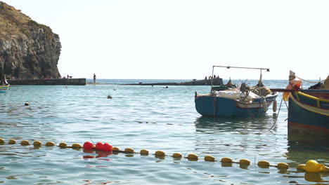 Yellow-buoy-line-and-colorful-boats-in-a-sea-bay,rocky-cliffs,Malta