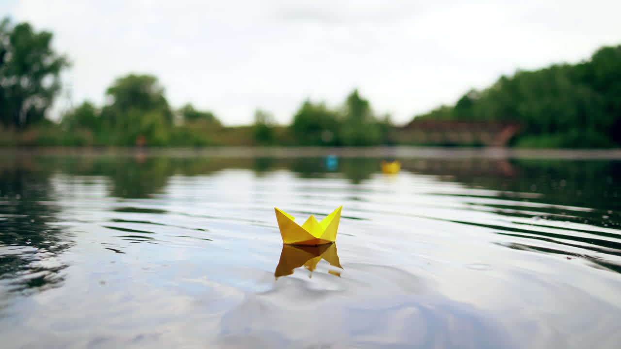Yellow paper boat is sailing on water surface under the evening sky. Origami ship made of yellow paper is swimming on the river at sunset.