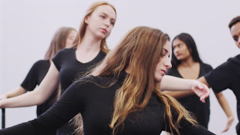 male and female students at performing arts school rehearsing ballet in dance studio using barre