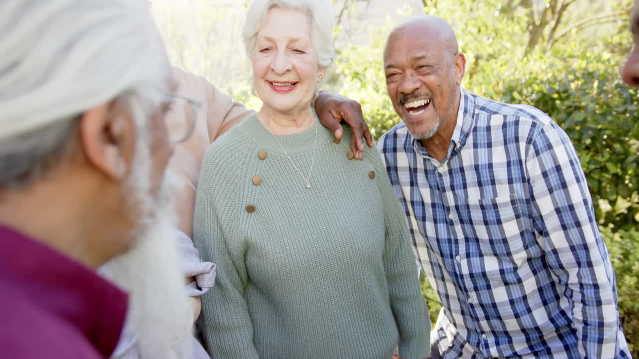 다양한 행복한 고령 여성과 남성 친구들이 빛 정원에서 포옹하고 웃고, 느린 동작