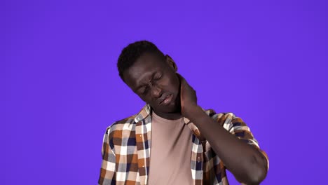 Young-african-american-man-in-plaid-shirt-having-neck-pain-or-super-tired,-face-grimace.-Isolated-over-blue-background