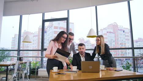 male boss with beard sits in front of laptop. members of office team leaned over the businessman to propose ideas and discuss them.
