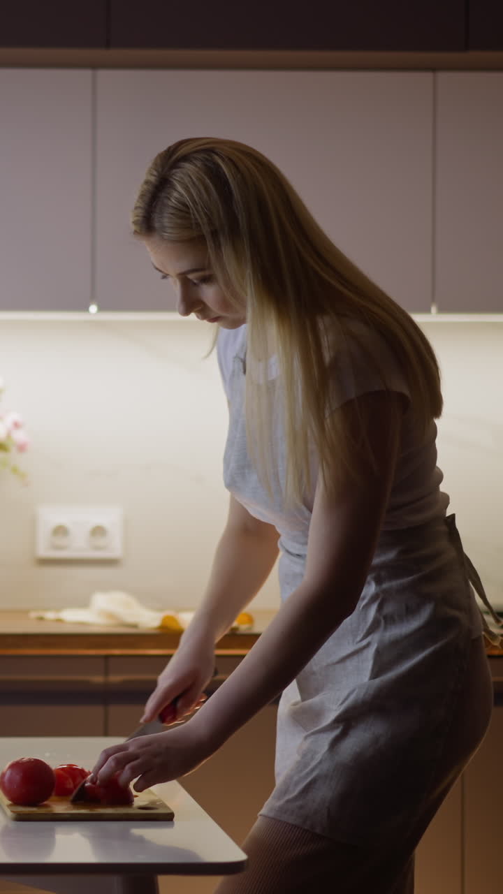 mujer rubia corta tomate rojo maduro para hacer una sabrosa ensalada para la cena en una tabla de madera de pie en la mesa en la cocina decorada vista lateral en cámara lenta
