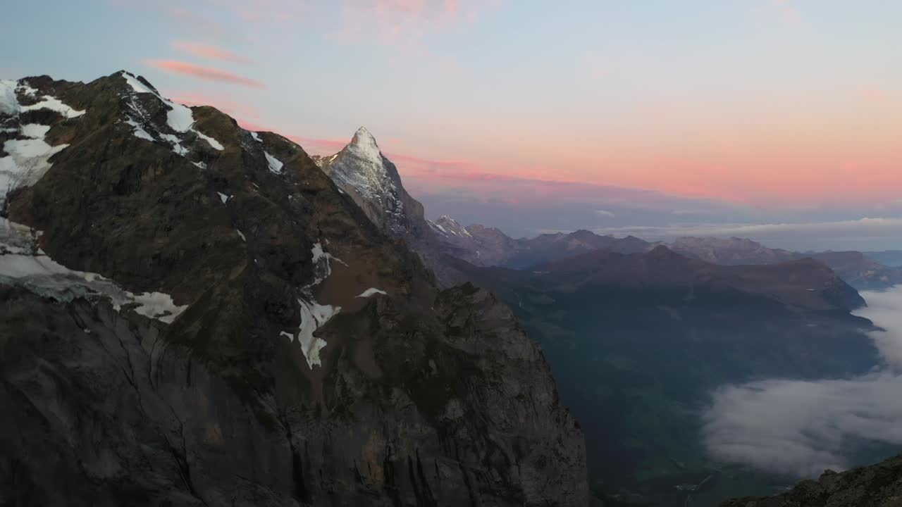 tiro aéreo lento y suave volando junto a la cima de las montañas alpinas en suiza durante un amanecer con colores rojo, naranja y rosa en el cielo