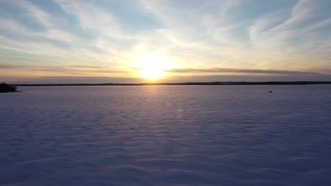 Puesta-De-Sol-Sobre-Un-Vasto-Lago-Congelado-Cubierto-De-Nieve-Con-Cabañas-De-Pesca-En-Hielo-Durante-El-Invierno