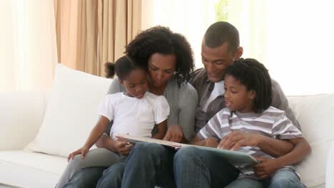 padres afroamericanos y niños leyendo un libro en la sala de estar