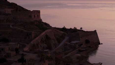 orange last light glow on ocean reflects off historic fortress ruins as boat leaves island