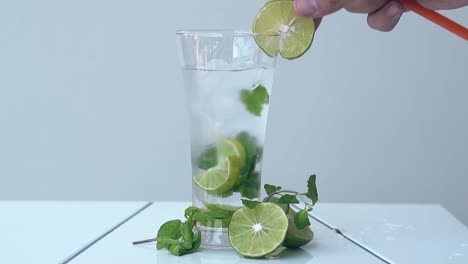 man-hand-puts-lime-slice-on-glass-edge-on-white-table