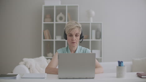 una mujer anciana especialista está consultando en línea trabajando desde casa usando una computadora portátil con internet y auriculares en interiores