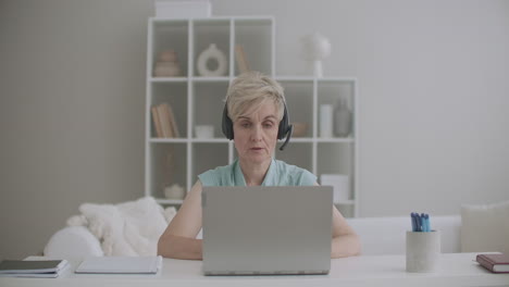 aged woman specialist is consulting online working from home using laptop with internet and headphones indoors shot