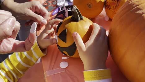 Una-Niña-Pequeña-Colocando-Pegatinas-En-Una-Calabaza-Naranja-En-Un-Festival,-De-Cerca