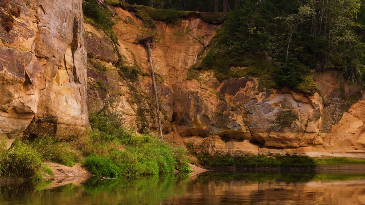 Detailed view of Erglu cliffs and a calm reflective riverbank in Gauja National Park, Latvia.