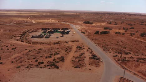 toma estática aérea del campamento militar de tiendas de campaña en medio del interminable desierto junto a una carretera vacía con un solo soldado caminando por ella