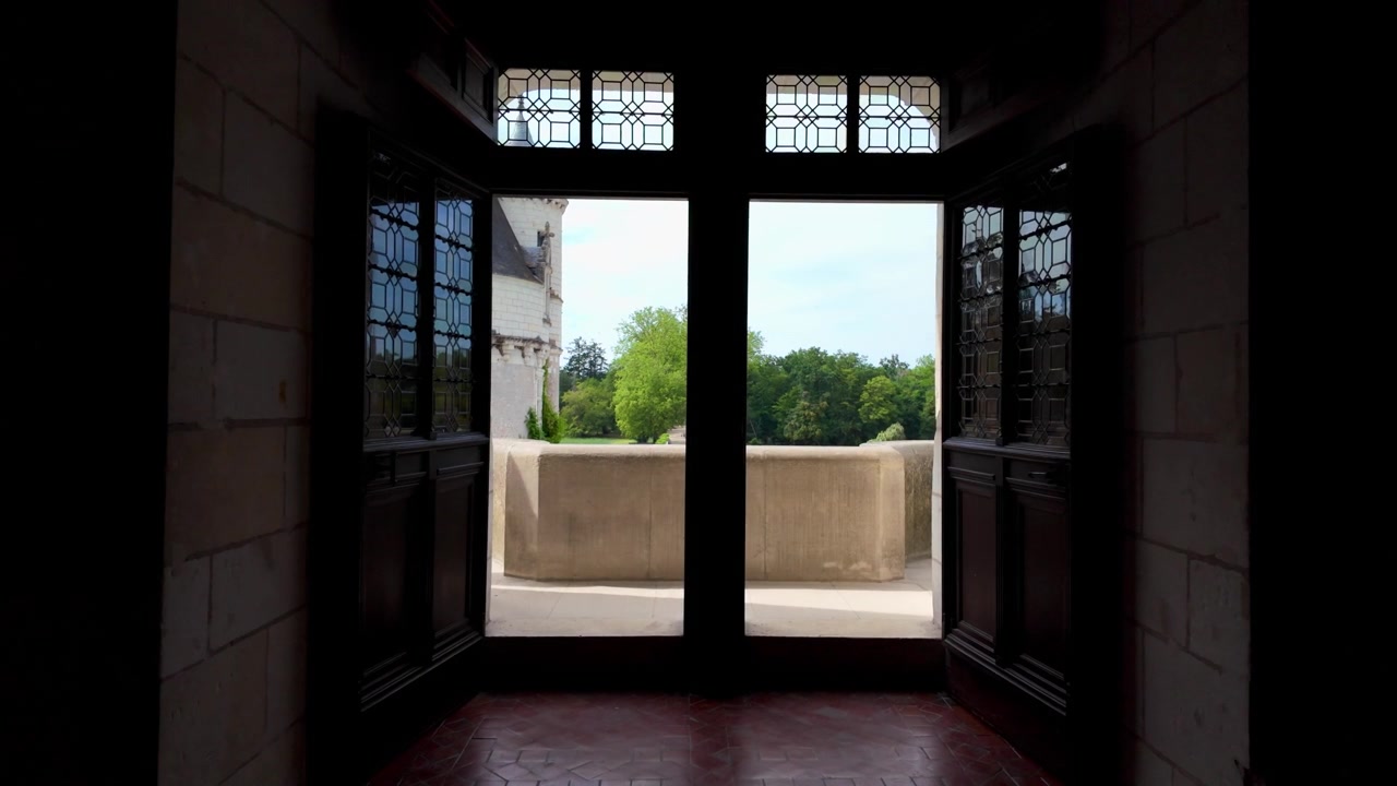 Elegant wooden doors open from the interior of Château de Chenonceau onto a stone balcony overlooking the castle grounds.