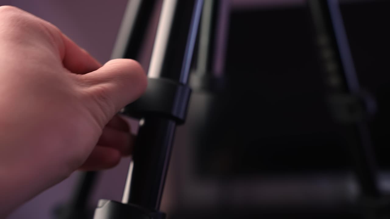 Close-up hand shortening tripod leg and tightening clamp, adjusting height for a stable camera setup in a studio