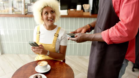 a young biracial woman is paying with a smartphone an african american worker