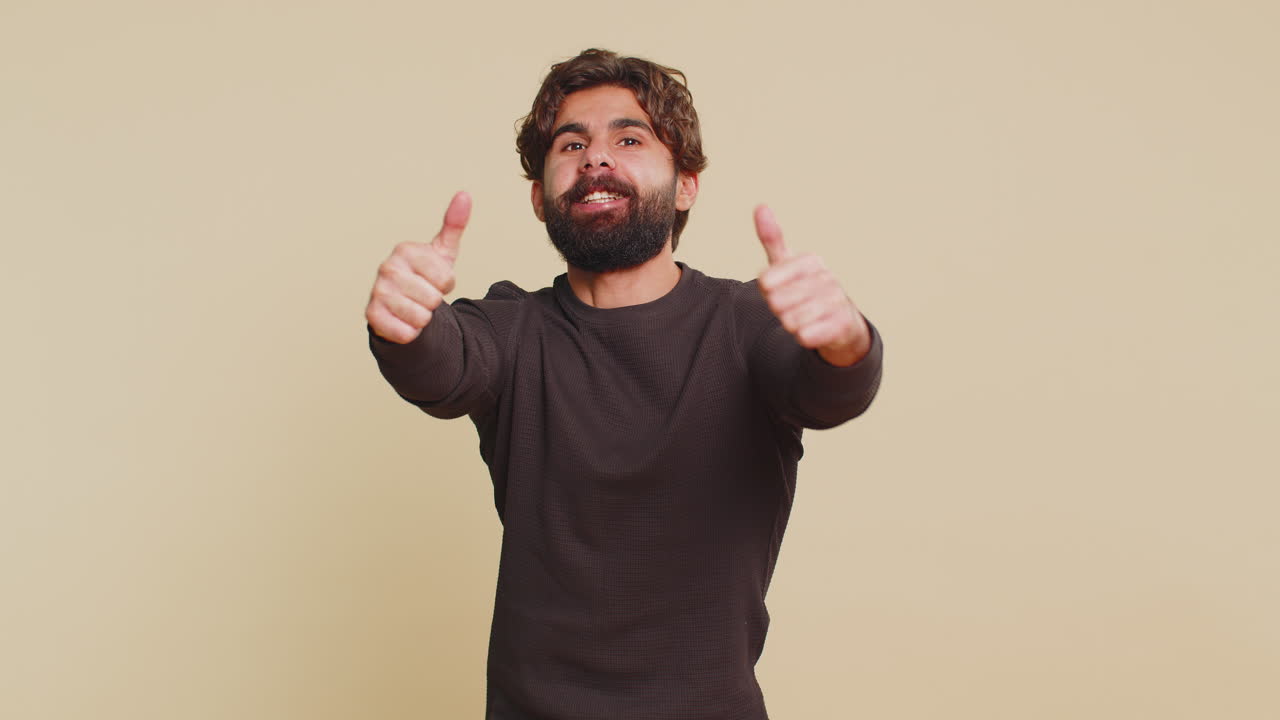 Happy man raises thumbs up agrees with something and gives positive reply against beige background
