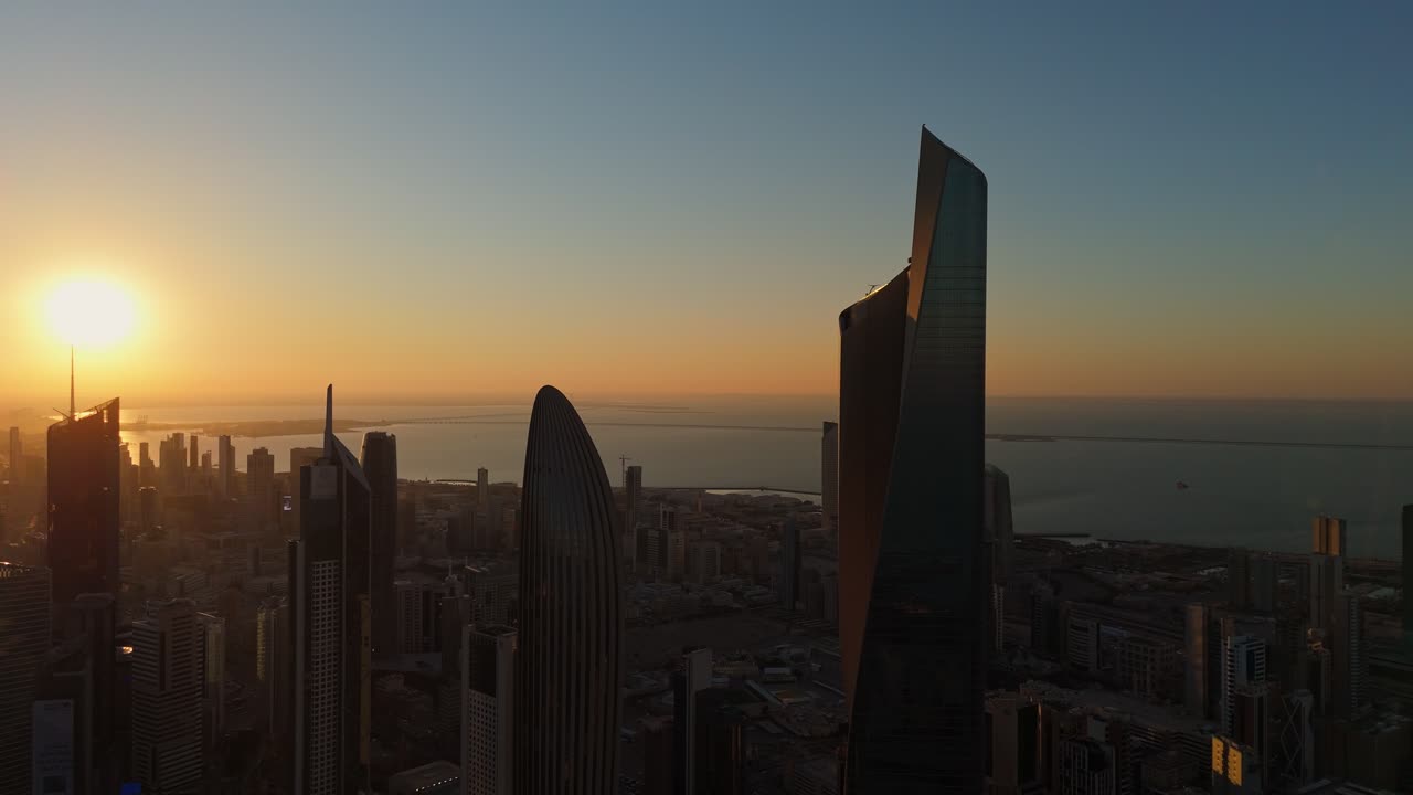 Breathtaking 4K aerial view of Kuwait City skyline at sunrise, capturing golden light on modern towers and calm sea. Ideal for cinematic visuals, travel, or city transitions.
