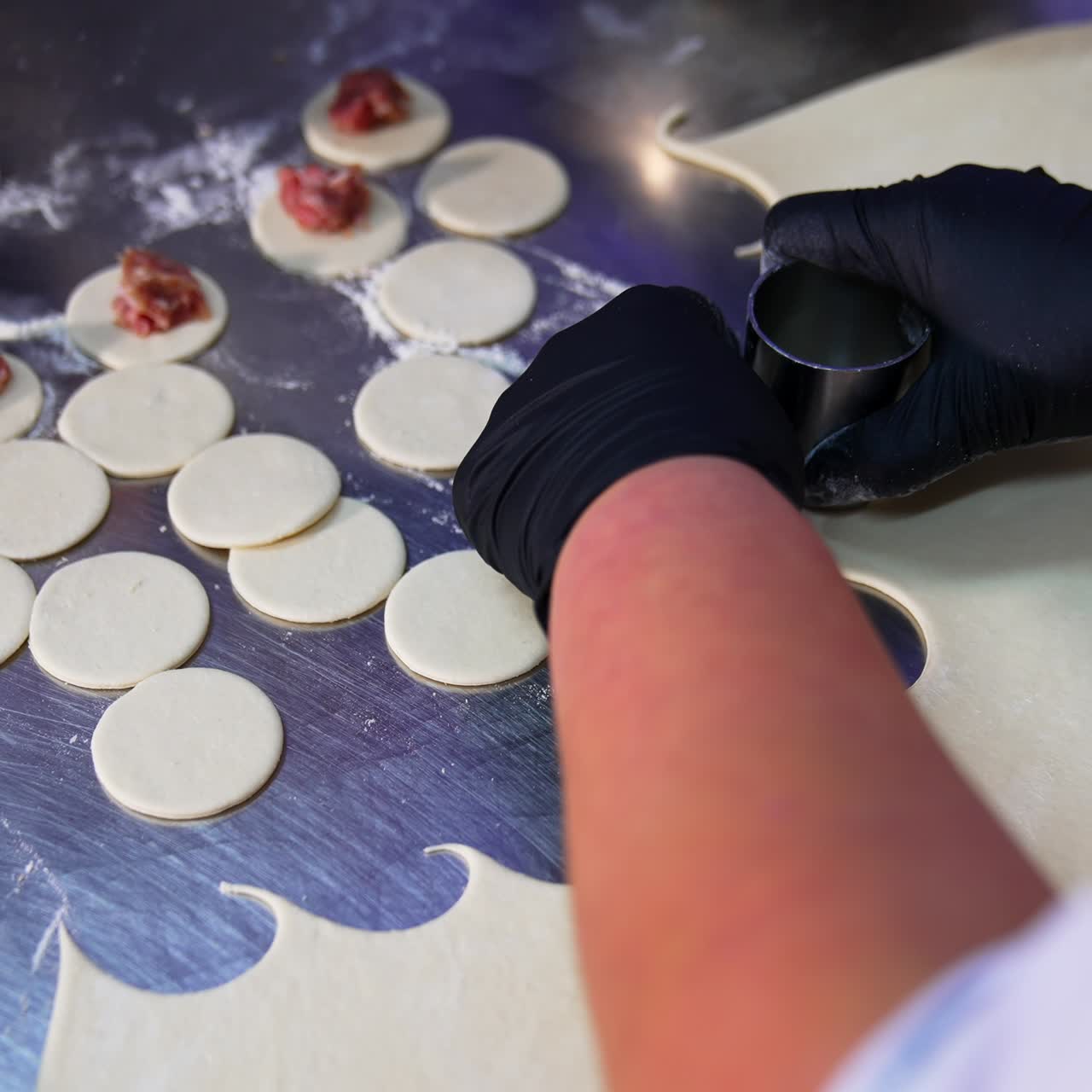 Hands in black latex gloves cut the little circles from duff. Worker lays the minced meat on top of the circles. Close up