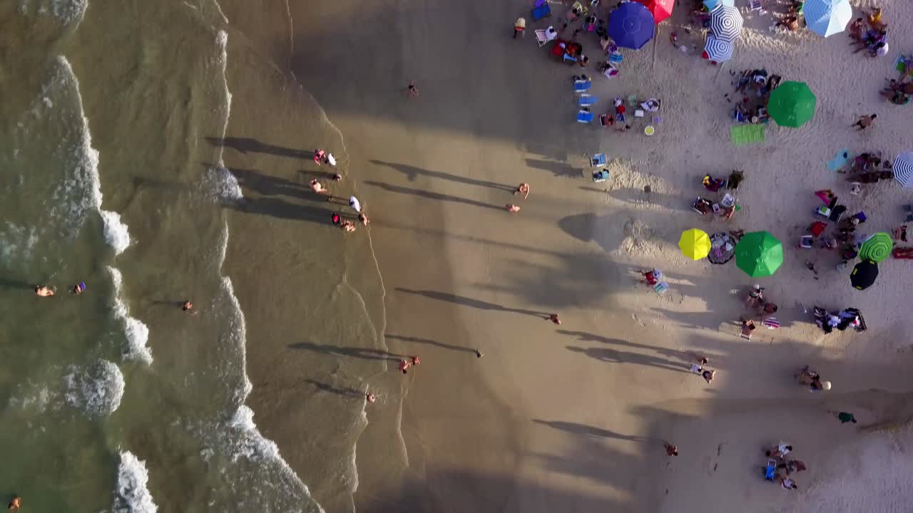 toma aérea de arriba hacia abajo volando sobre personas disfrutando de una hermosa playa a la hora dorada