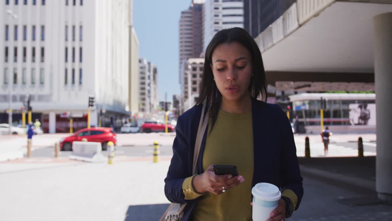 African american woman holding coffee and using smartphone in street
