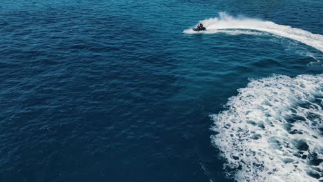 Two-people-are-riding-water-scooter,-jet-ski,-making-circles-and-rotating-moves-on-water-surface,-attractive-aerial-view,-captured-near-the-coastline-of-Ibiza,-Spain