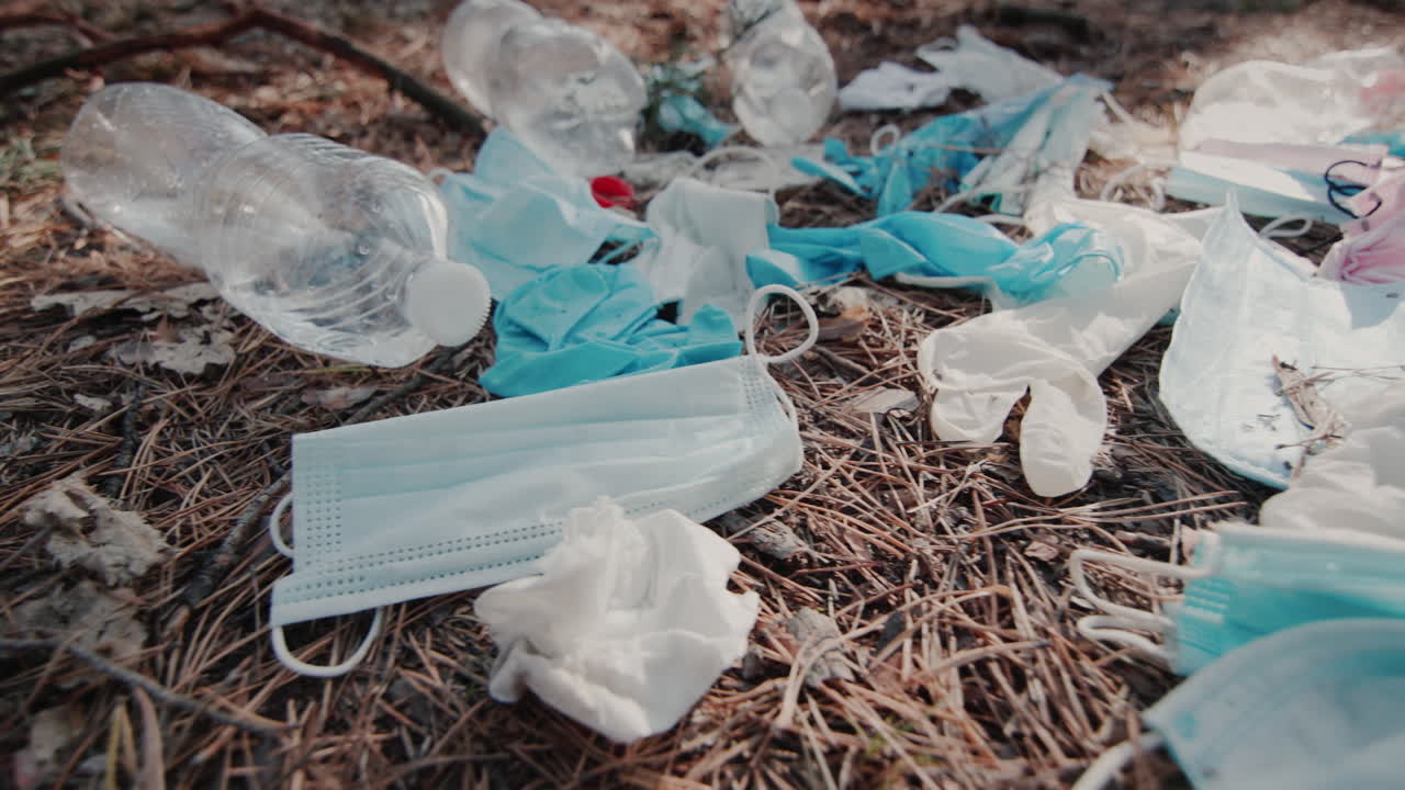 많은 중고 의료용 마스크와 기타 잔해가 숲의 바닥에 놓여 있습니다.