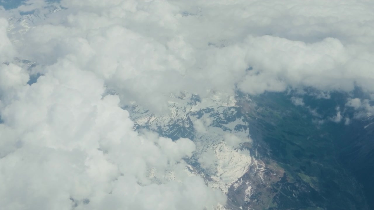Finestrino aereo, ripresa aerea di montagne invernali innevate e nuvole, ripresa in movimento. Vista passeggero ad alta quota a 60fps che guarda in basso una vasta catena di ghiacciai e una fitta coltre bianca.