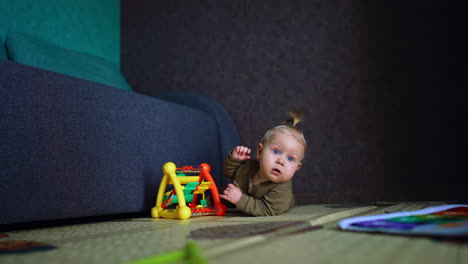 caucasian infant with blond hair lies on the floor looking up with surprise. little kid with a bright toy.