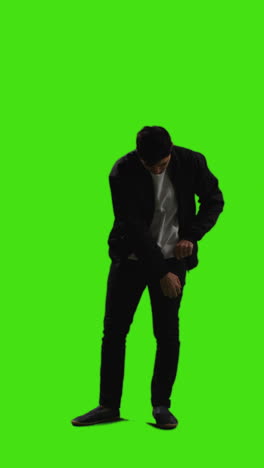 Vertical-Video-Full-Length-Shot-Of-Young-Man-Answering-Call-On-Mobile-Phone-Standing-Against-Green-Screen-With-Low-Key-Lighting