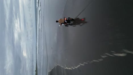 vertical format aerial overtakes motorcyclists on expansive sand beach