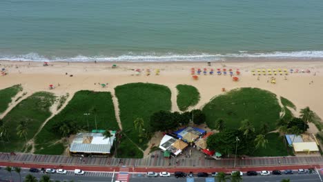 Right-trucking-aerial-drone-shot-of-the-famous-tourist-destination-Cabo-Branco-beach-in-the-tropical-capital-city-of-Joao-Pessoa-in-Paraiba,-Brazil-with-vibrant-tents-lined-up-for-visitors