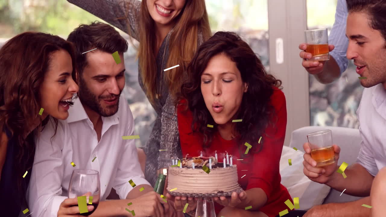 Celebrating birthday, woman blowing out candles on cake with group cheering