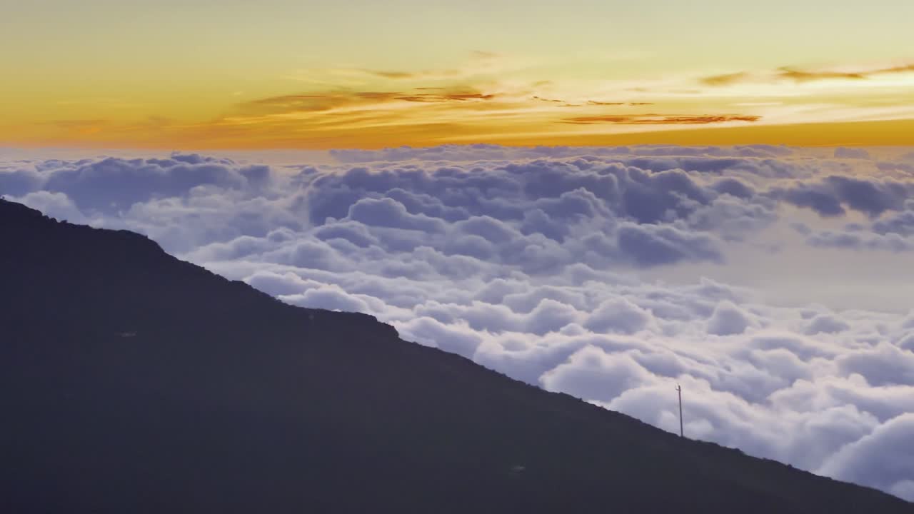Cinematic panning shot from rolling clouds to the Haleakala Observatory during sunset at the summit of Haleakala in Maui, Hawai'i