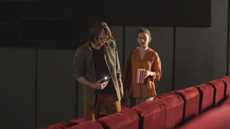 pareja entrando a un cine y encontrando asientos usando la linterna del teléfono antes de que comience la película 1