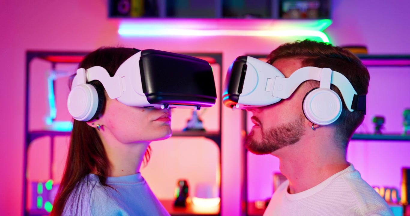 Giovane coppia che indossa visori VR e tiene in mano controller in una stanza illuminata al neon