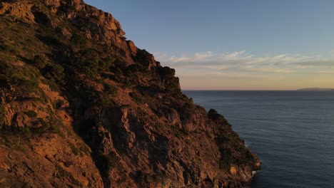 imágenes de drones de un acantilado costero iluminado por la puesta de sol, de aspecto irregular, a lo largo de la costa del mar mediterráneo