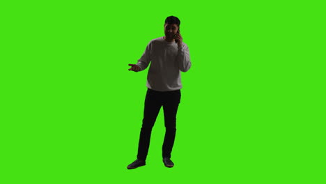 young man talking on mobile phone standing against green screen with low key lighting 3