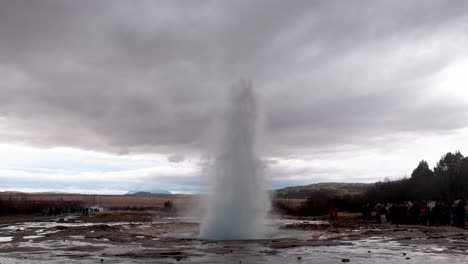 tourists at the great geysir eruption with gloomy sky in southwestern iceland