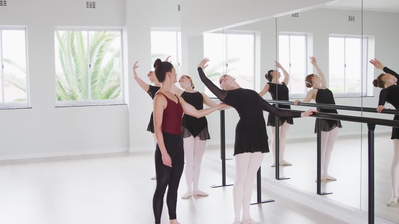 bailarinas de ballet caucásicas ejercitándose con una barra junto a un espejo durante una clase de ballet