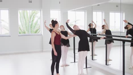 caucasian ballet female dancers exercising with a barre by a mirror during a ballet class