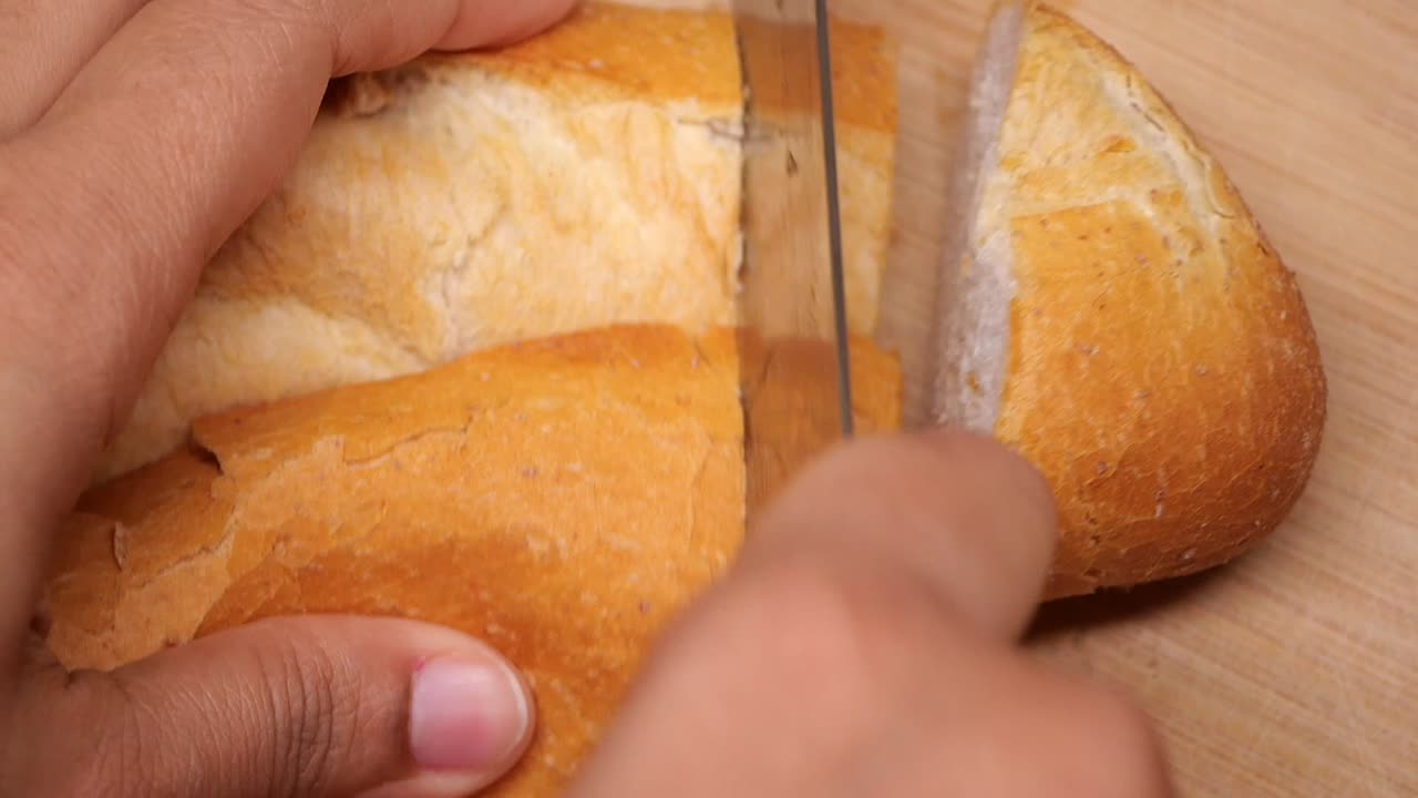 Close-Up of Hand Slicing Fresh Bread on a Wooden Board