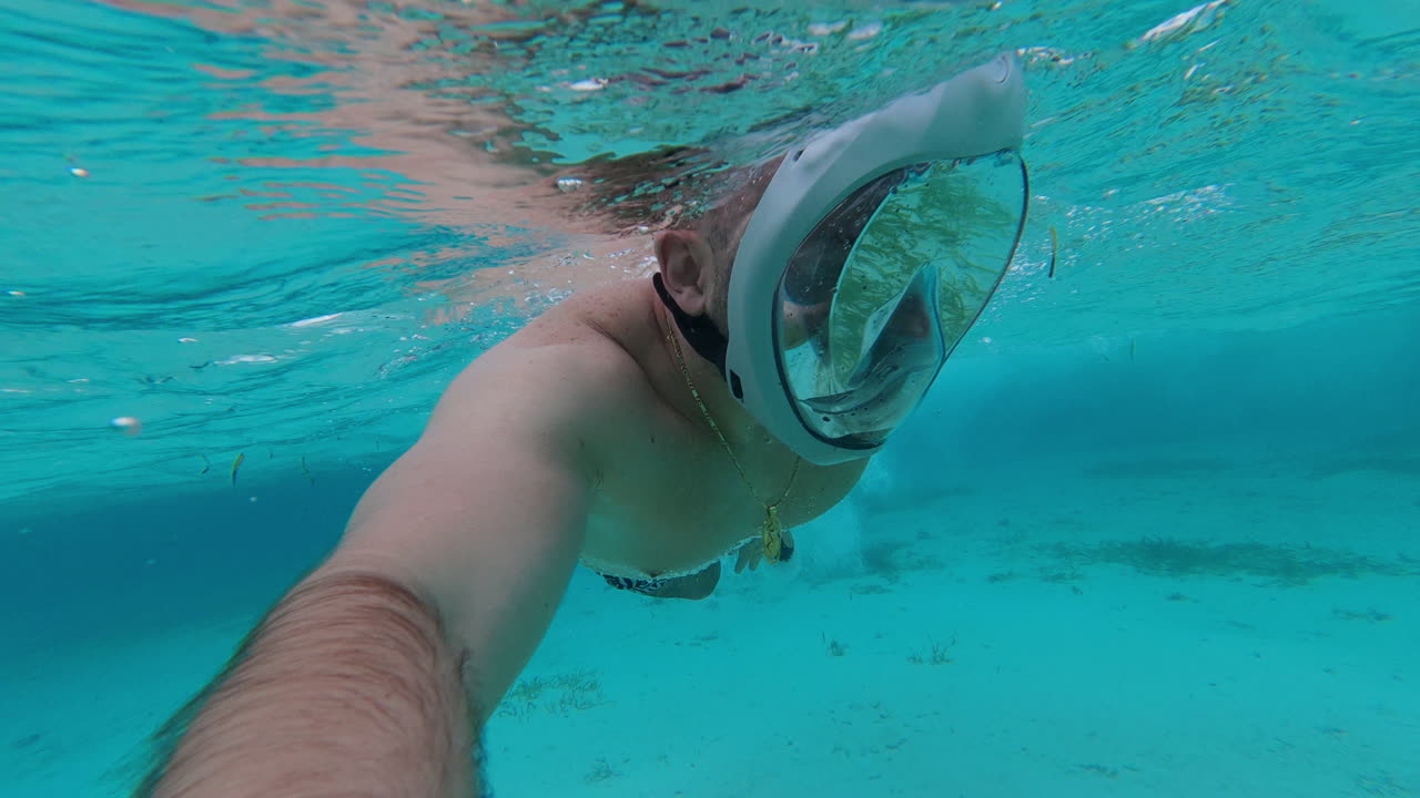 Handheld underwater selfie shot of a man wearing a snorkeling mask swimming in the clear turquoise ocean water during a sunny day