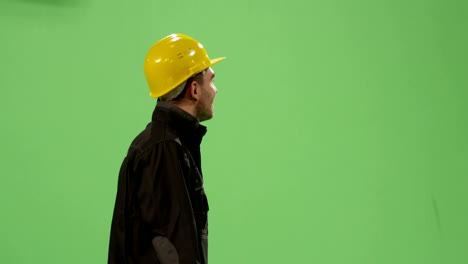 construction worker in a hard hat is walking on a mock-up green screen in the background.