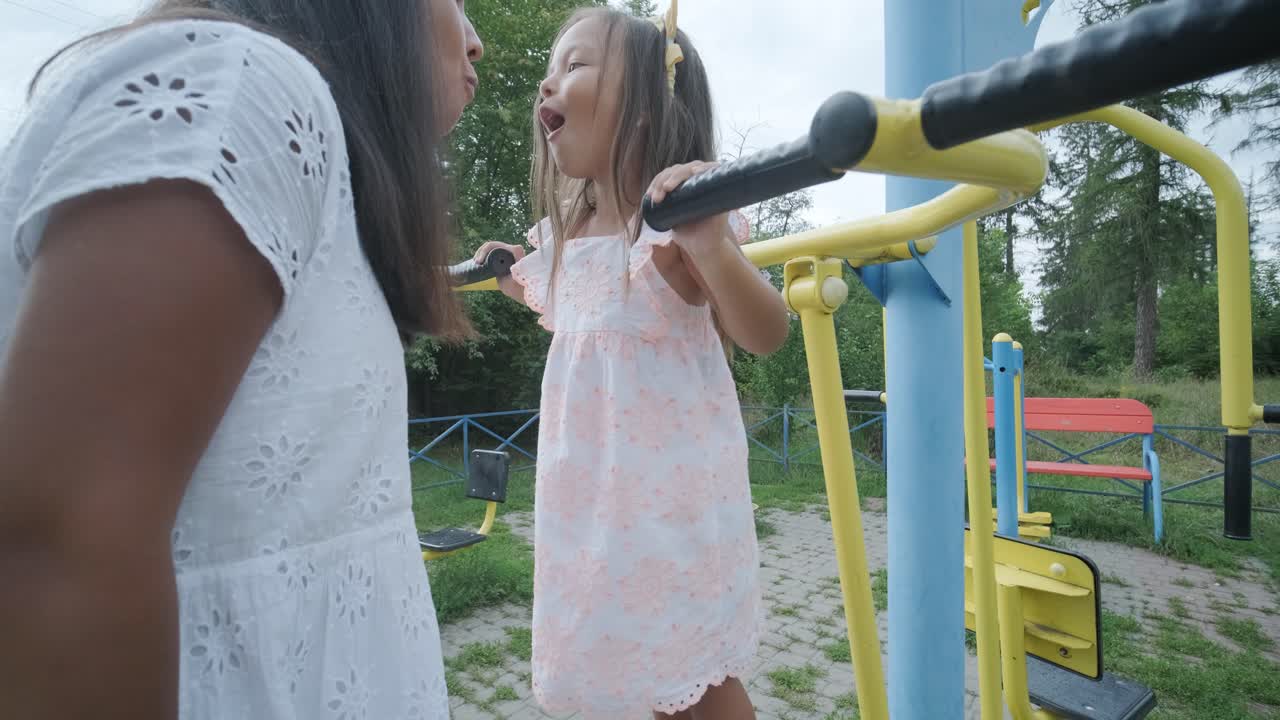 una madre embarazada y su hija joven disfrutan de un tiempo de juego juntos en un patio de recreo en el parque, rodeados de árboles y vegetación