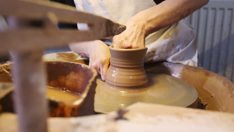 close up of male potter shaping clay for pot on pottery wheel in ceramics studio